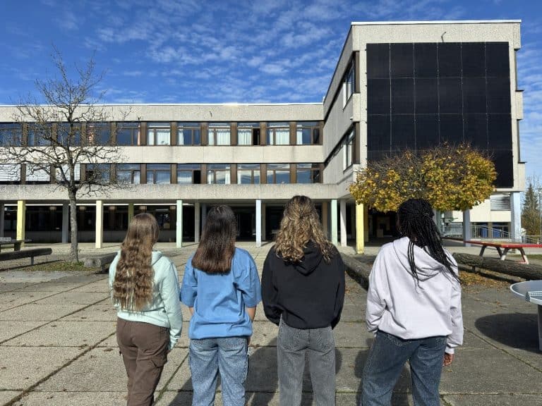 Vier Schülerinnen in Schulmerch blicken auf das ASG Schulgebäude
