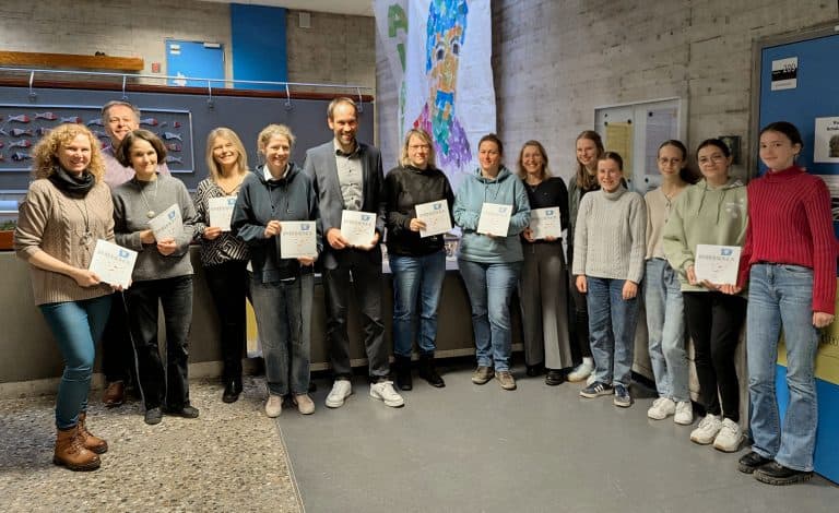 Verschiedene Persönlichkeiten der Schule posieren lächelnd mit einer PRISMA-Ausgabe für die Kamera.